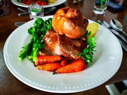 A plate of roast beef with Yorkshire pudding, carrots, and broccoli.
