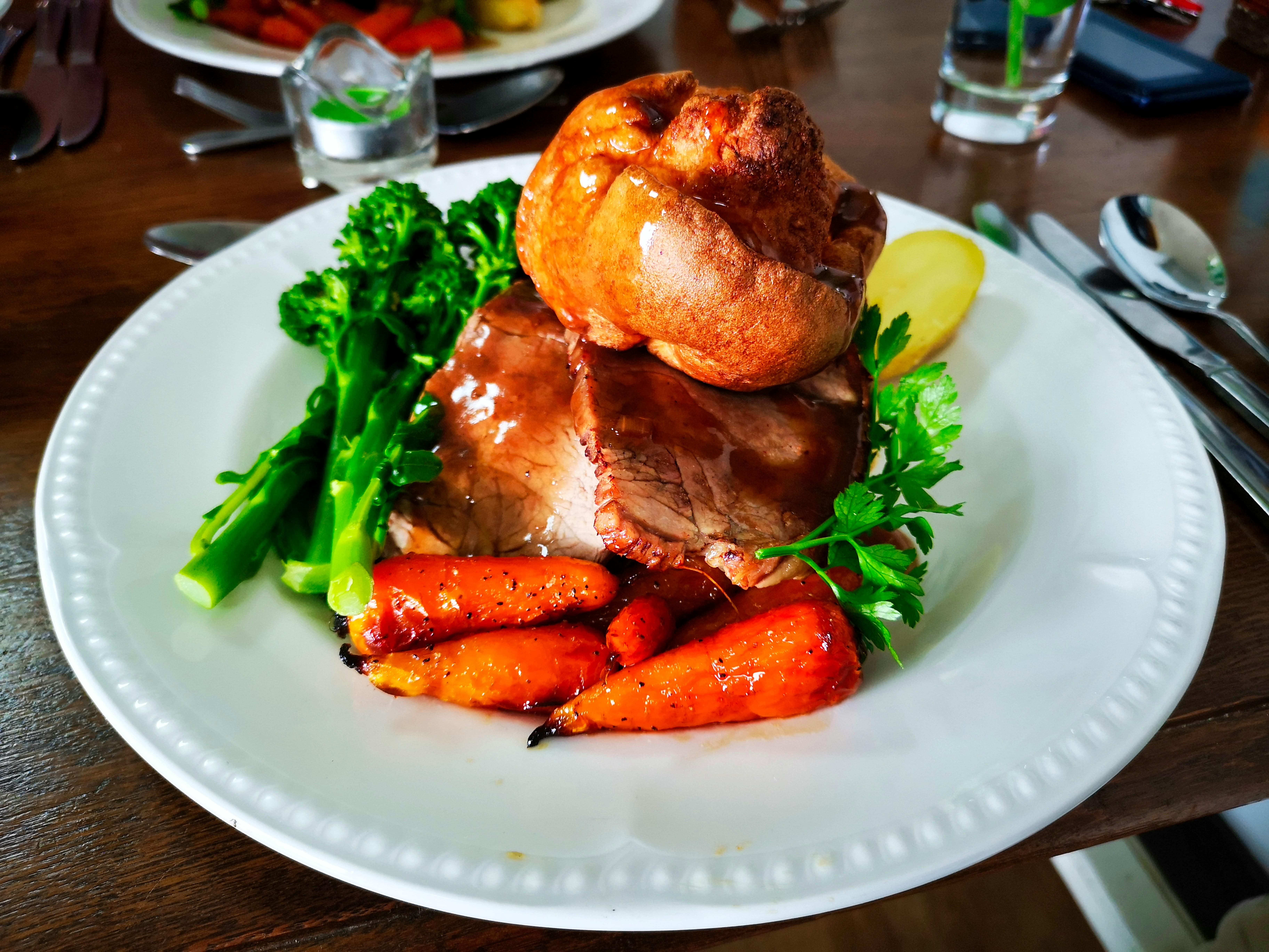 A plate of roast beef with Yorkshire pudding, carrots, and broccoli.
