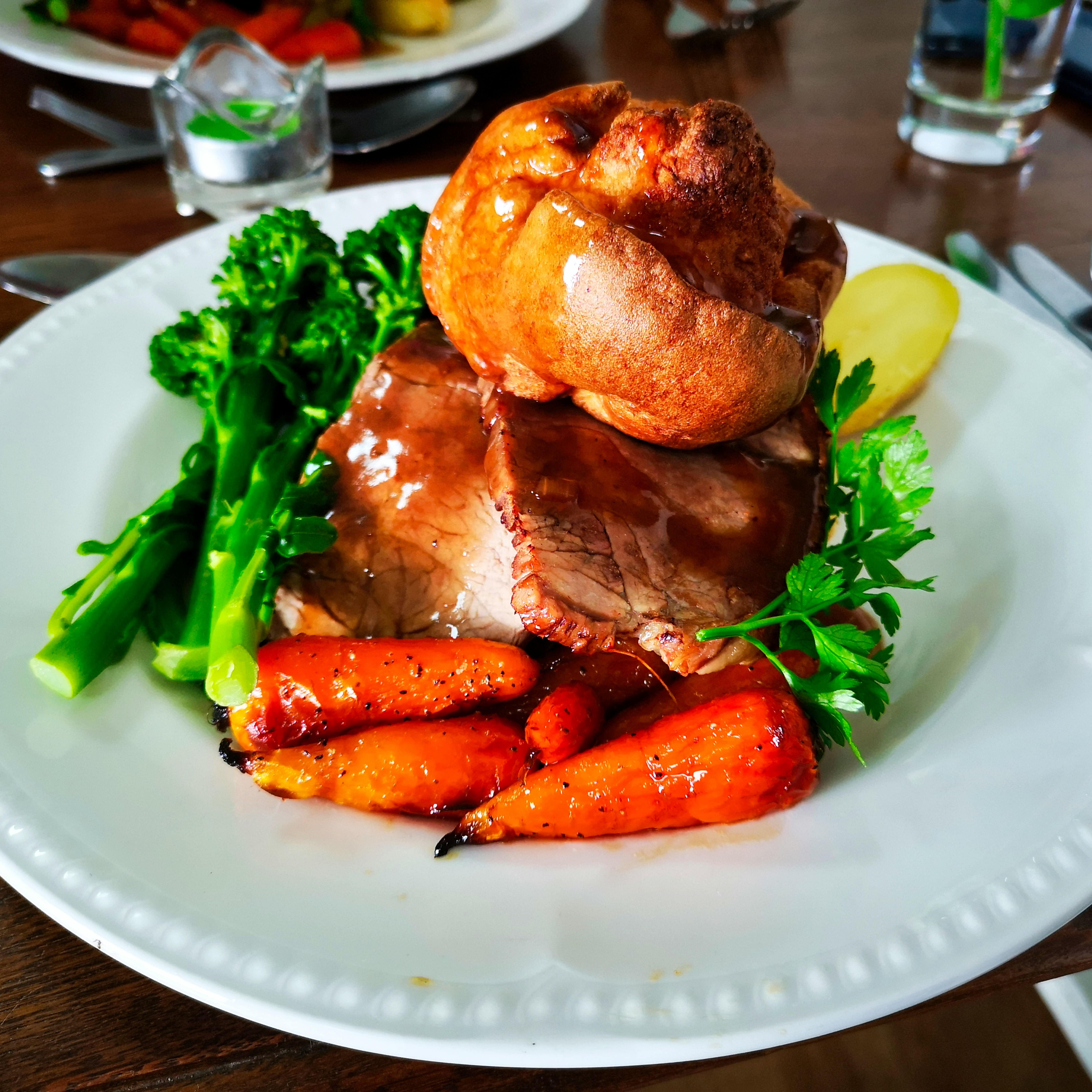 A plate of roast beef with Yorkshire pudding, carrots, and broccoli.