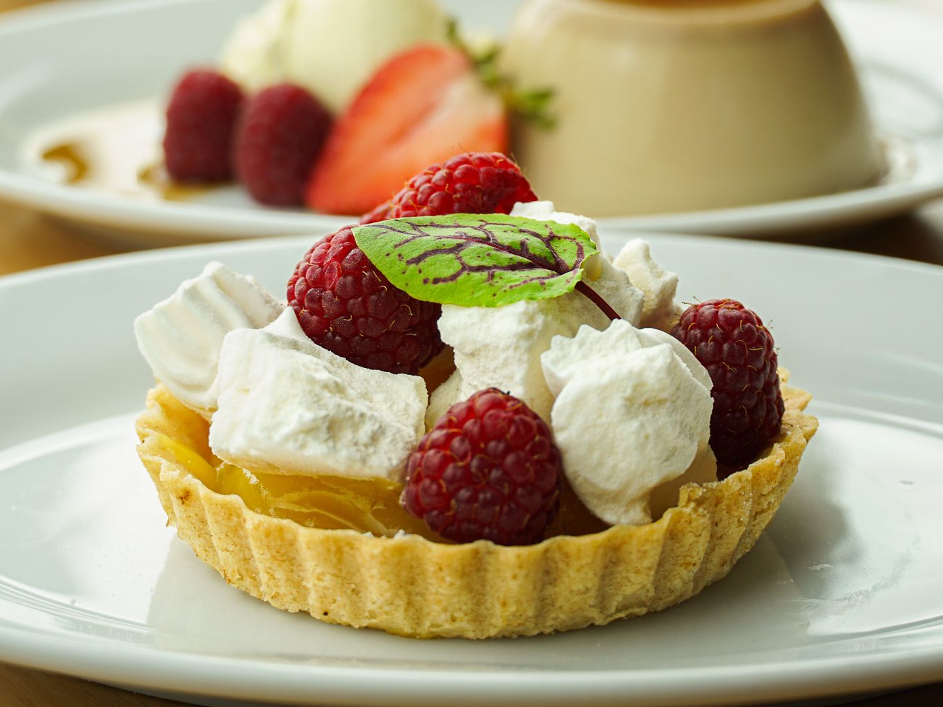 Assorted desserts including a raspberry tart, creamy flan with berries, and a layered parfait in a glass.