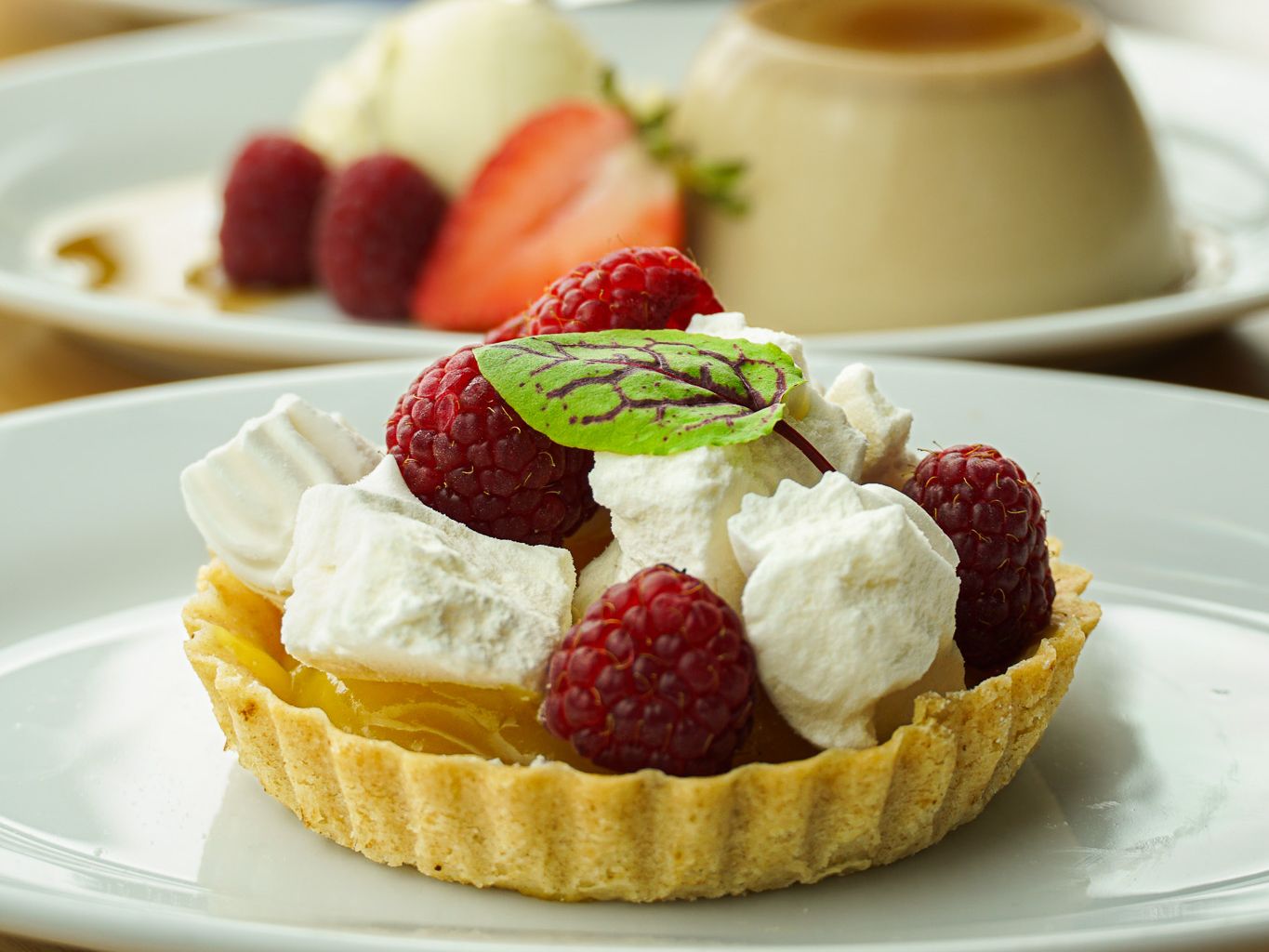 Assorted desserts including a raspberry tart, creamy flan with berries, and a layered parfait in a glass.