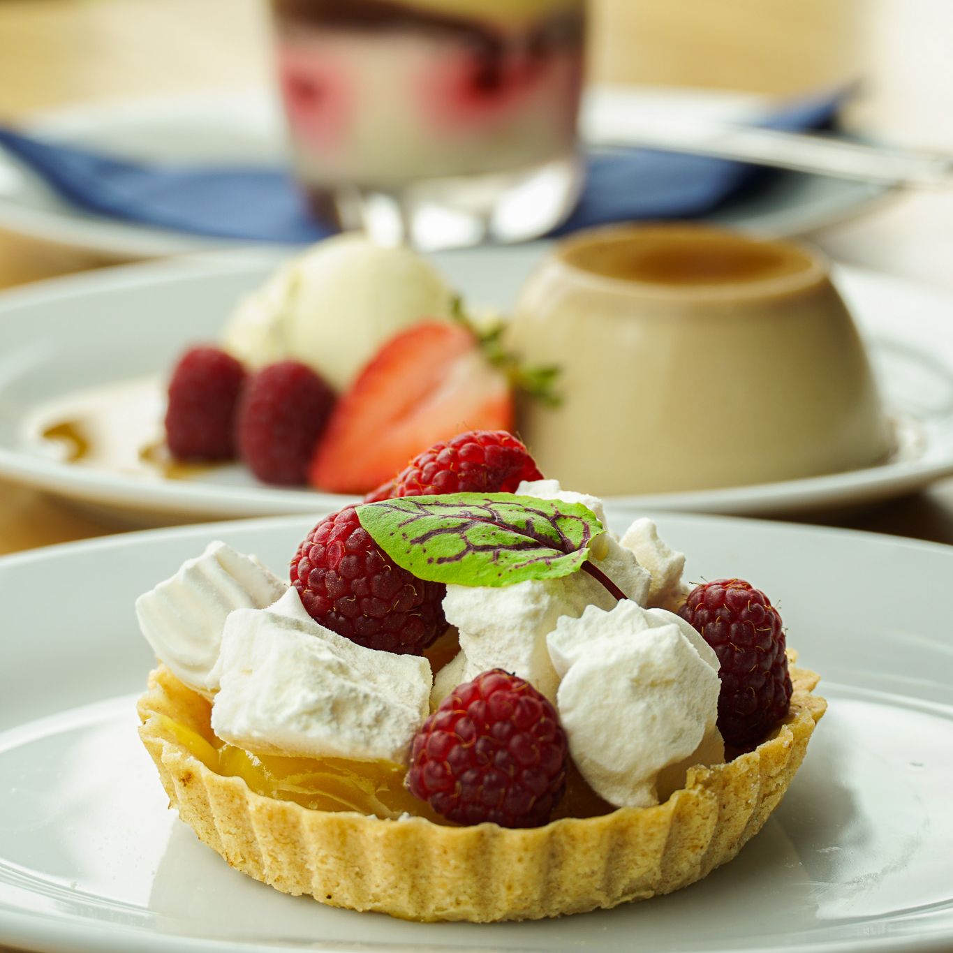 Assorted desserts including a raspberry tart, creamy flan with berries, and a layered parfait in a glass.