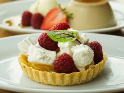 Assorted desserts including a raspberry tart, creamy flan with berries, and a layered parfait in a glass.