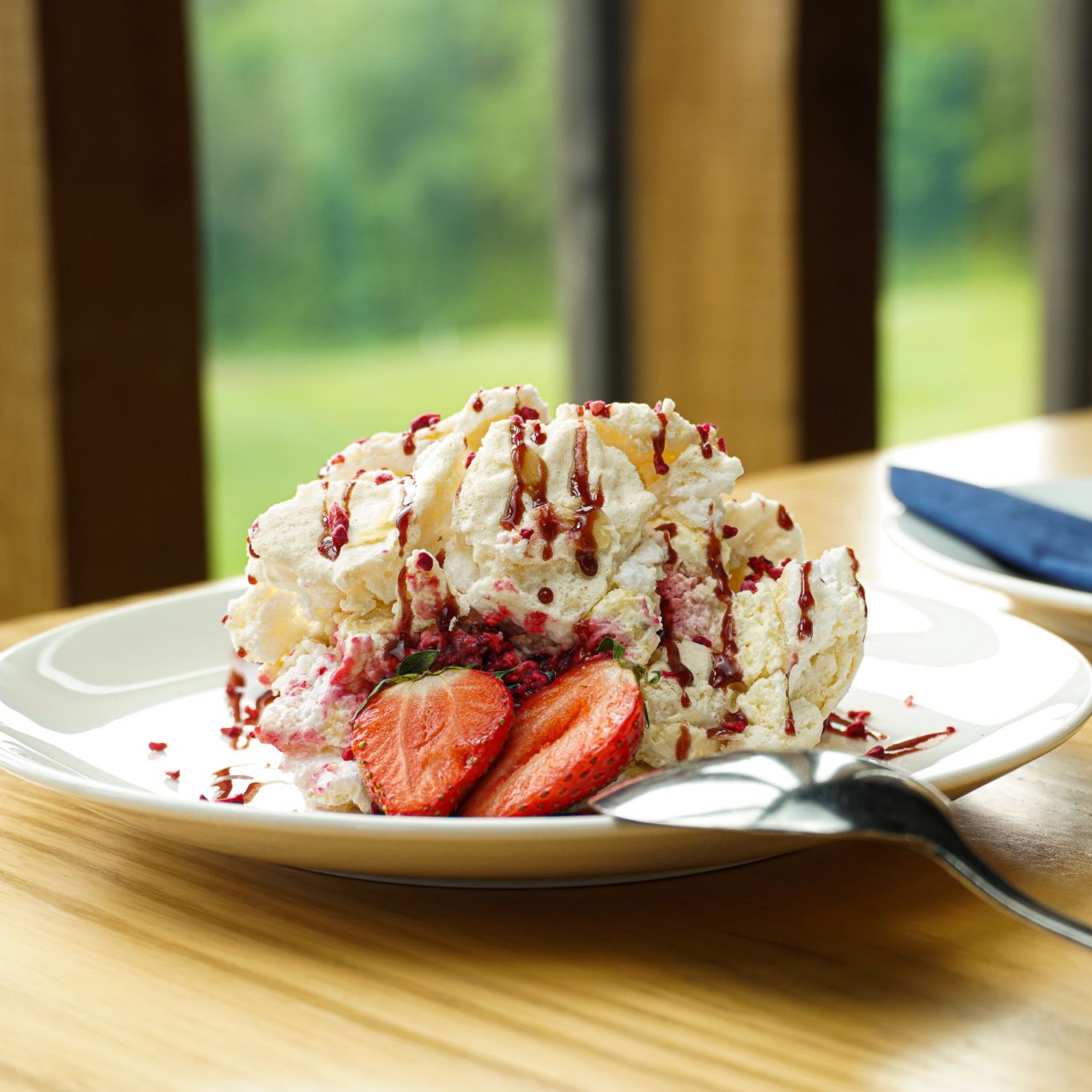 A plate of dessert with whipped cream, strawberries, and berry drizzle next to a glass of trifle dessert topped with strawberries