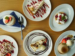 Assorted gourmet desserts including cakes, tarts, and panna cotta arranged on white plates
