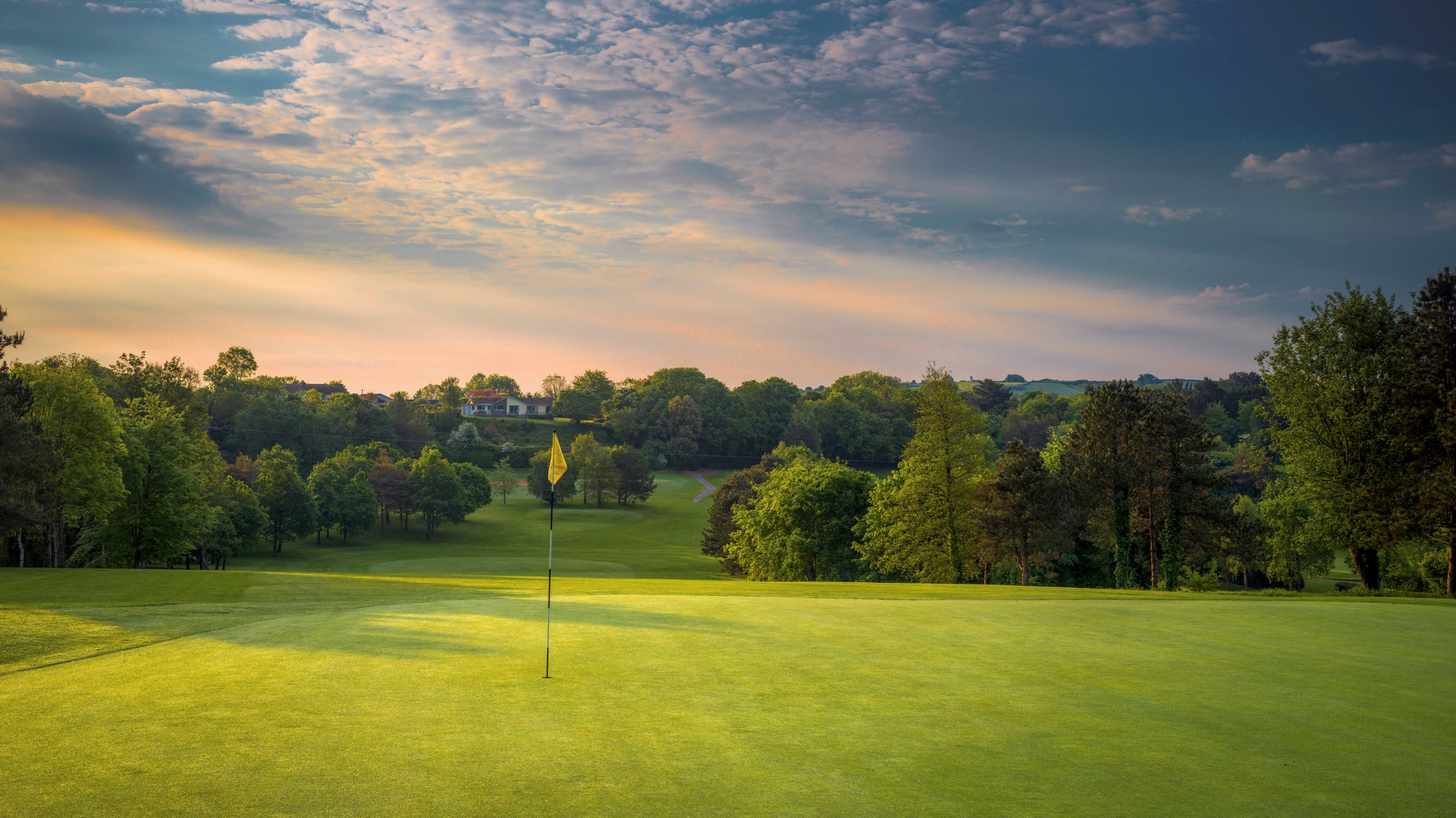 Golf flag on a green with lush trees and cloudy sky at sunset