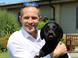 Smiling man holding a black dog outdoors on a sunny day