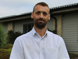 Man in white short-sleeved button-up shirt standing outside in front of a building