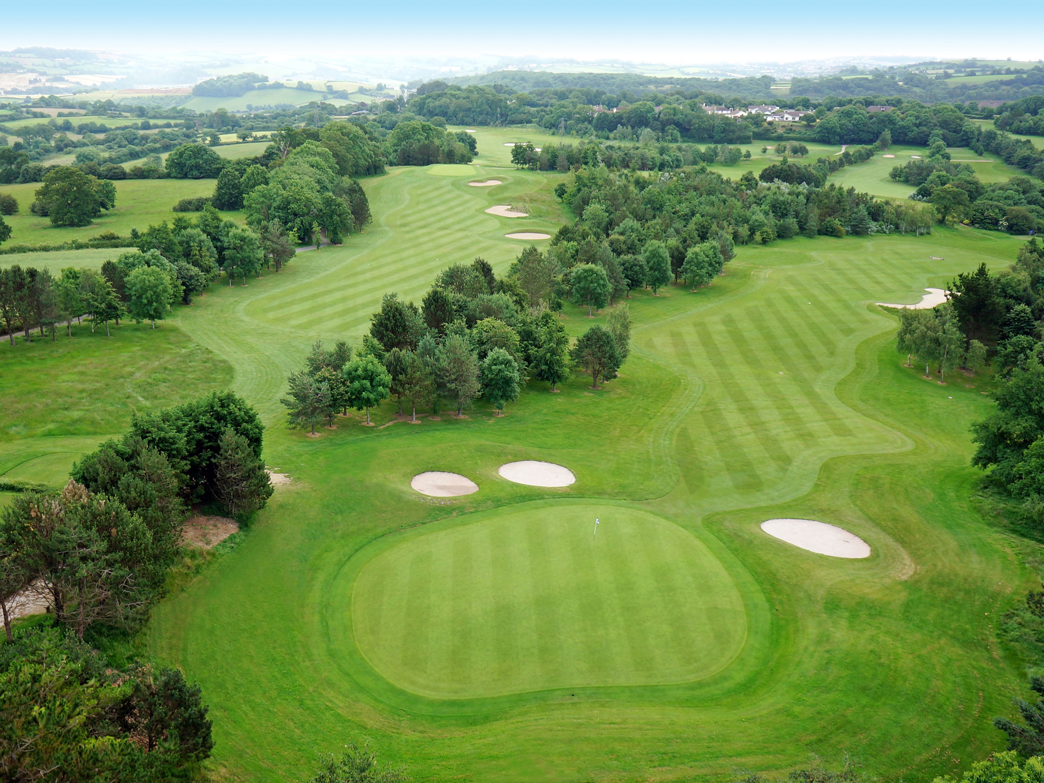 Aerial view of a lush, green golf course with sand bunkers and fairways surrounded by trees.