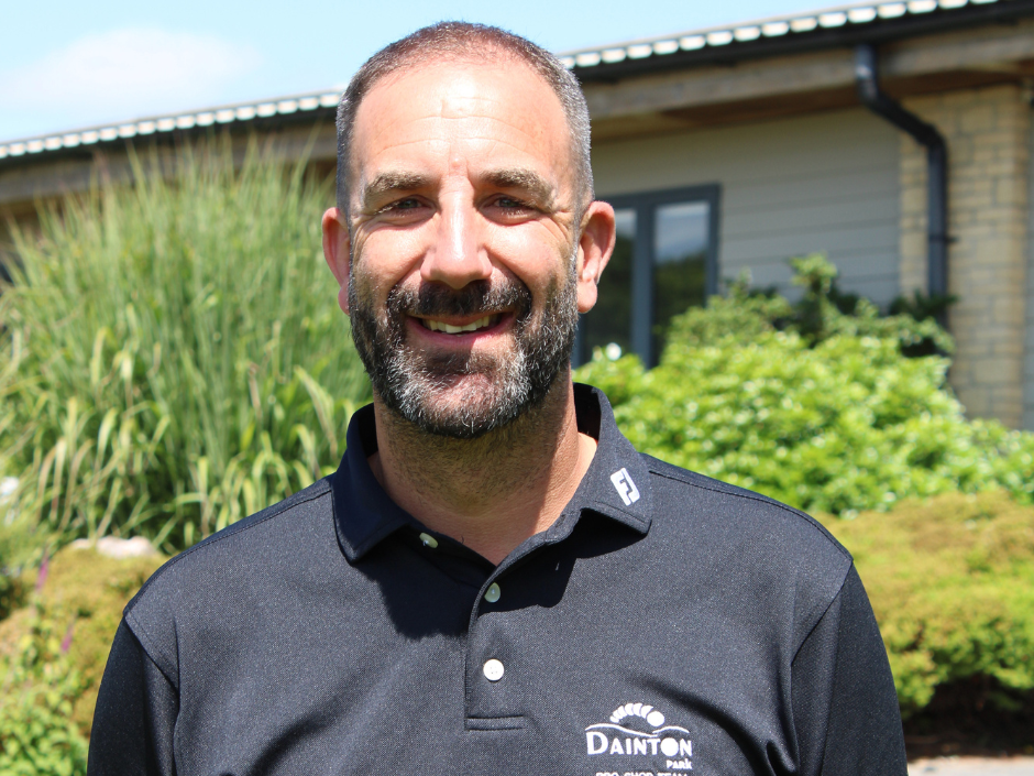 Smiling man wearing a black Dainton Park Pro Shop Team polo shirt standing outdoors