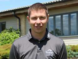 Man wearing a grey Dainton Park Pro Shop Team shirt standing outside in front of a building.