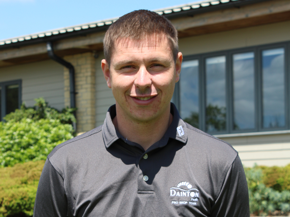 Man wearing a grey Dainton Park Pro Shop Team shirt standing outside in front of a building.