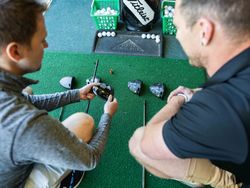 Two men examining golf club heads and shafts at an indoor golf facility.
