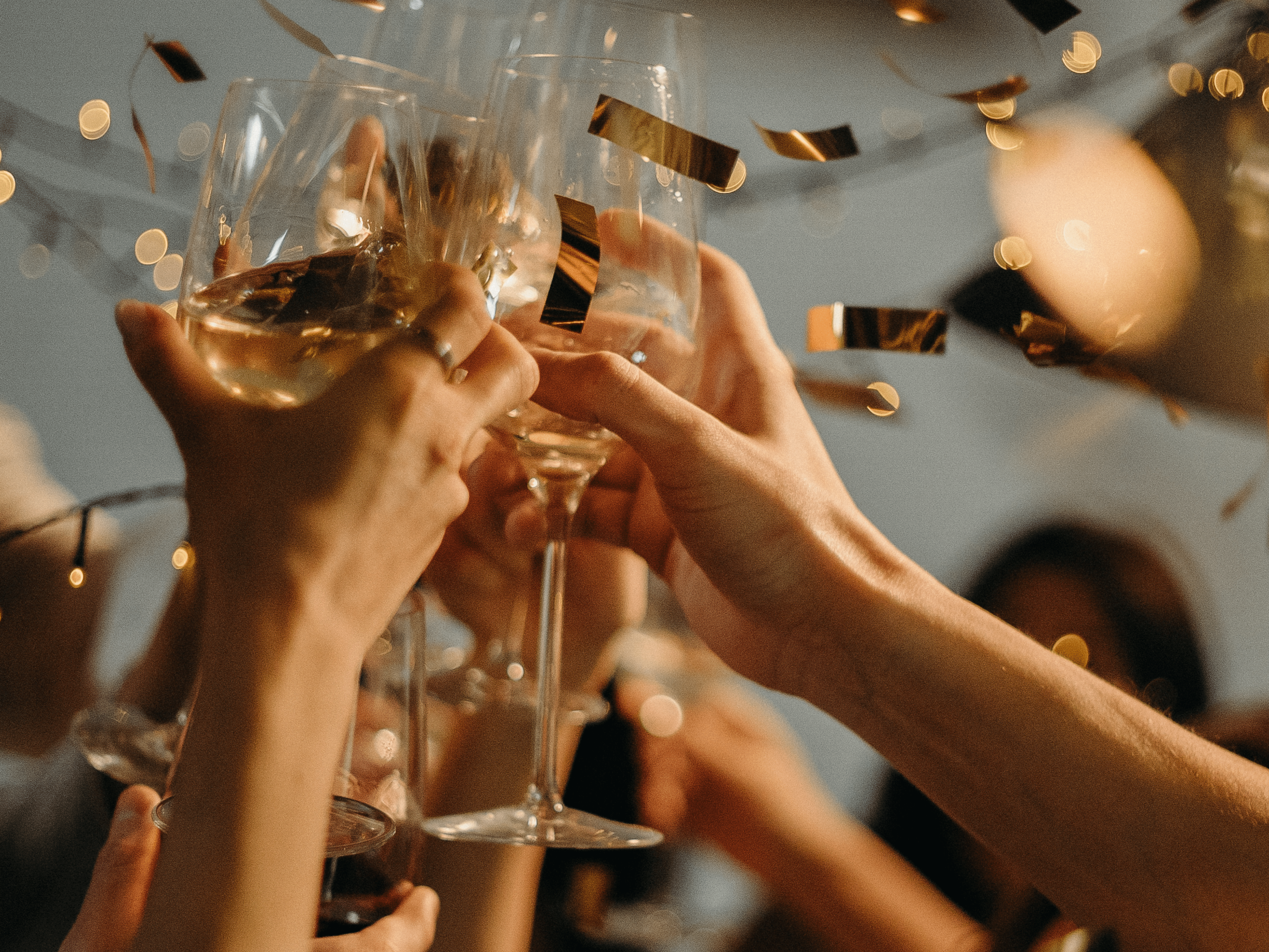 People toasting with wine glasses at a celebration with confetti falling