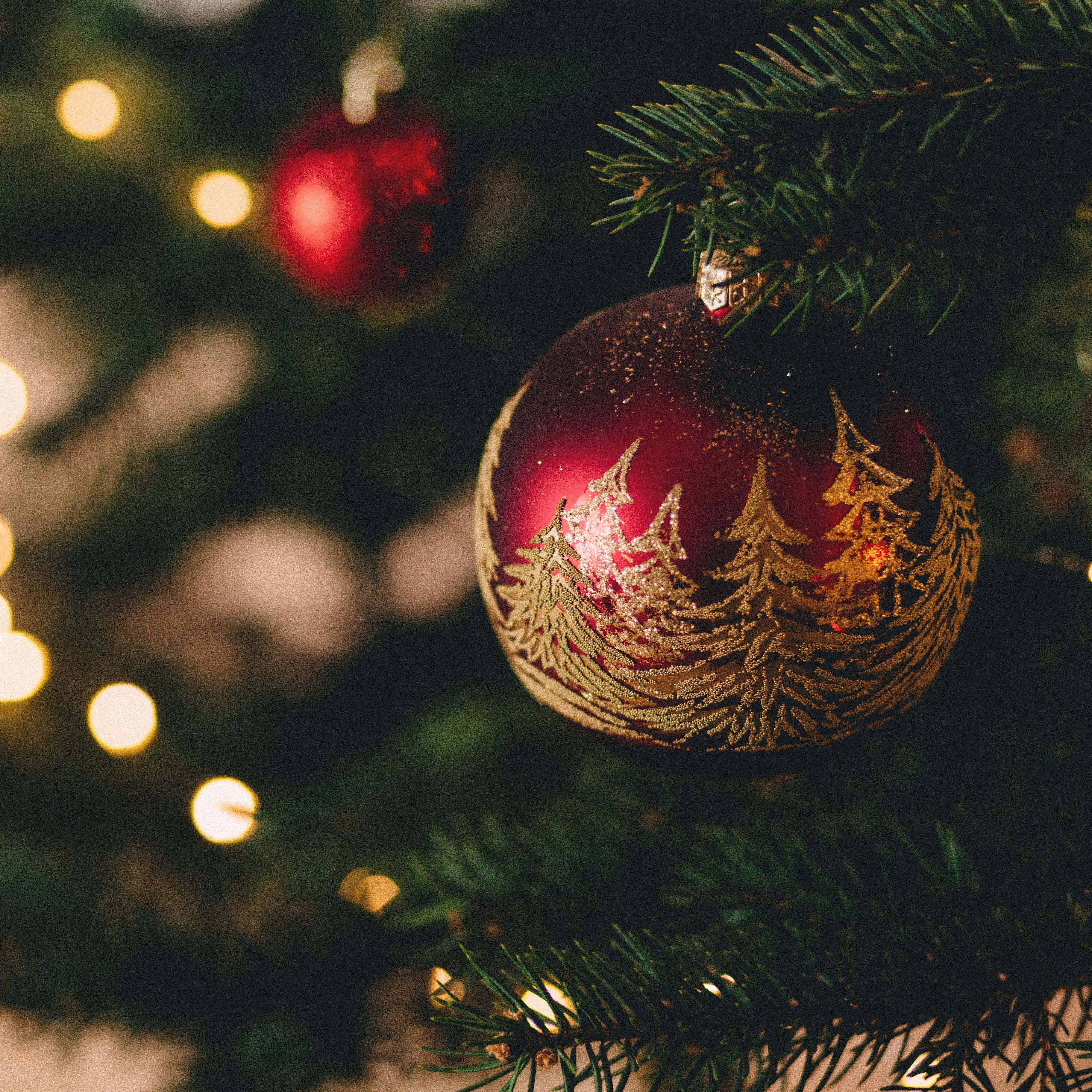 Close-up of a decorated Christmas tree ornament with gold trees on a red bauble and festive lights in the background