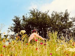 Person wearing a red helmet in a field of wildflowers with trees and blue sky in the background