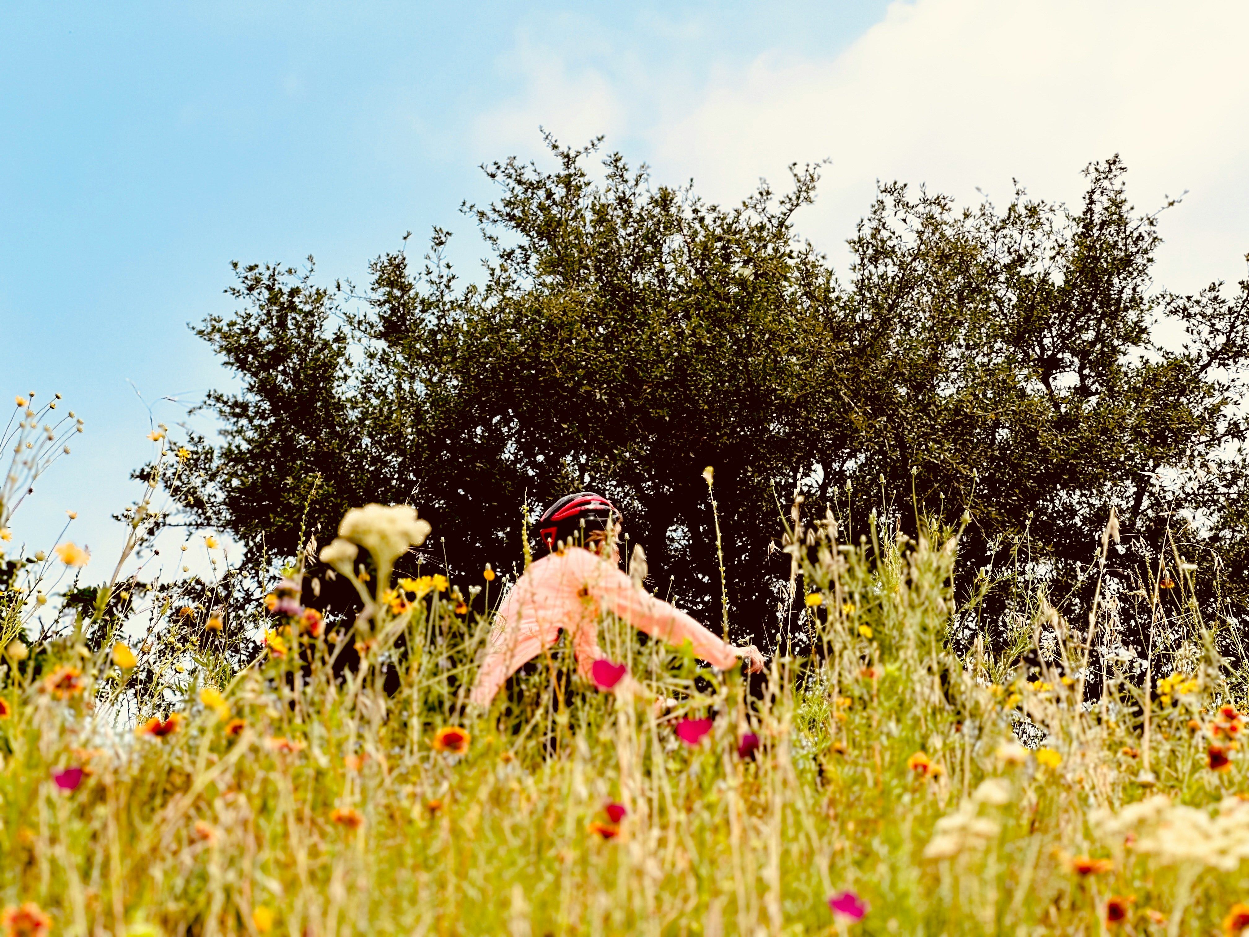 Person wearing a red helmet in a field of wildflowers with trees and blue sky in the background