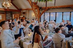 A large group of well-dressed guests at an indoor celebration raise their glasses for a toast.