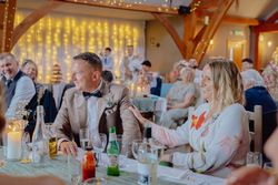 Smiling guests seated at a decorated table during a wedding reception, with fairy lights in the background
