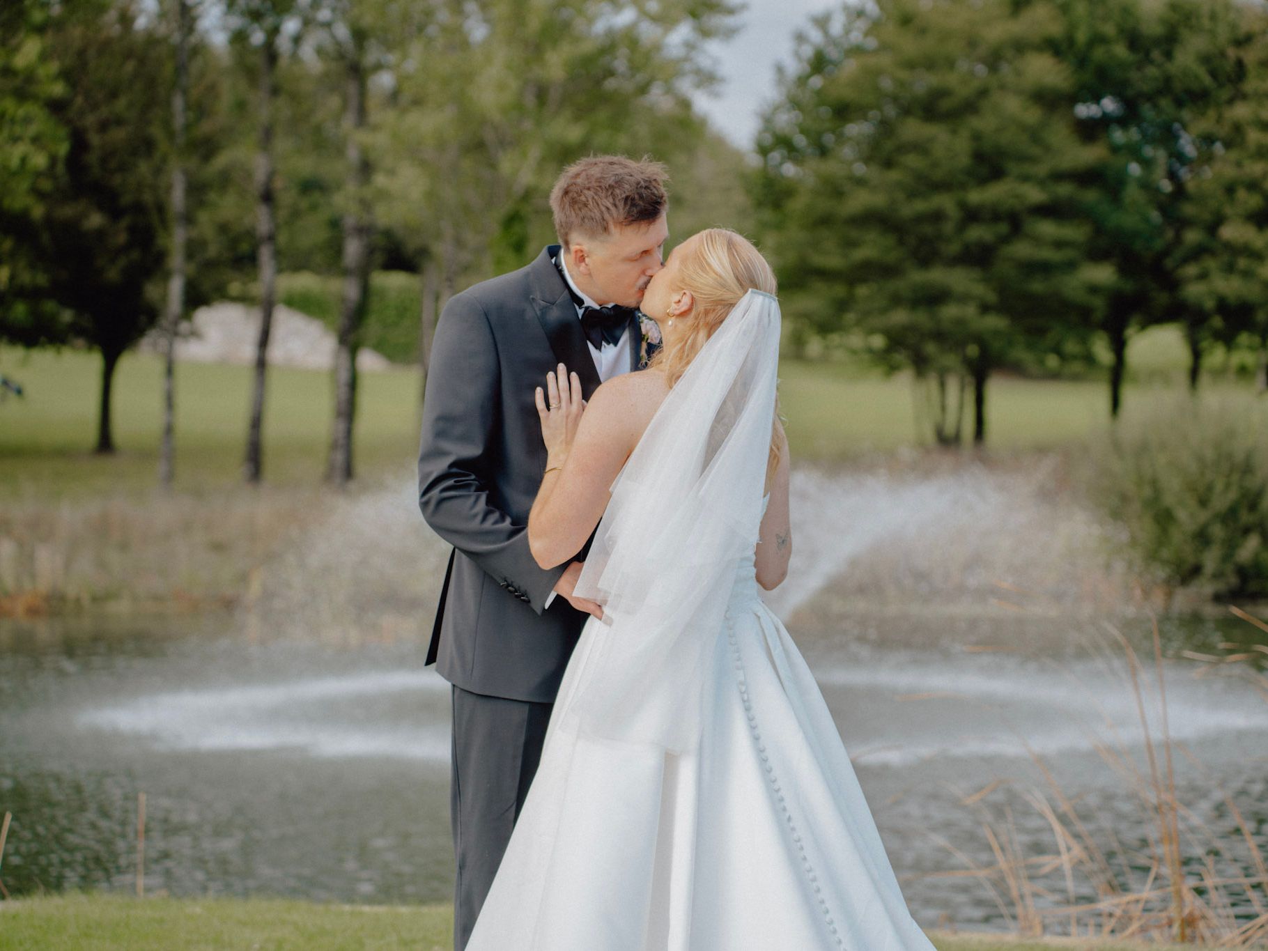 Bride and groom kissing in front of a pond with fountain