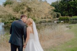 Bride and groom kissing by a pond with swans and trees in the background