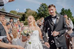 Bride and groom smiling and holding hands while wedding guests throw confetti outside.