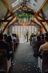 Indoor wedding ceremony with bride and groom standing at the altar beneath a large chandelier, surrounded by guests seated in a beautifully decorated wooden hall.