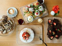 Assortment of baked goods and coffee on a wooden table, including brownies, cake with strawberries, scones, and lattes