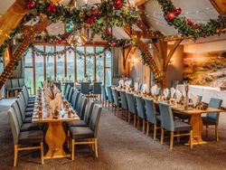 Elegant banquet hall decorated for Christmas with two long dining tables, blue chairs, and festive garlands hanging from wooden beams.