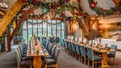 Elegant banquet hall decorated for Christmas with two long dining tables, blue chairs, and festive garlands hanging from wooden beams.