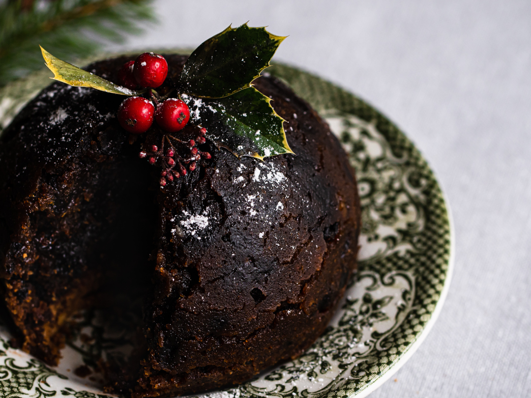 Traditional Christmas pudding topped with holly and berries on a patterned plate