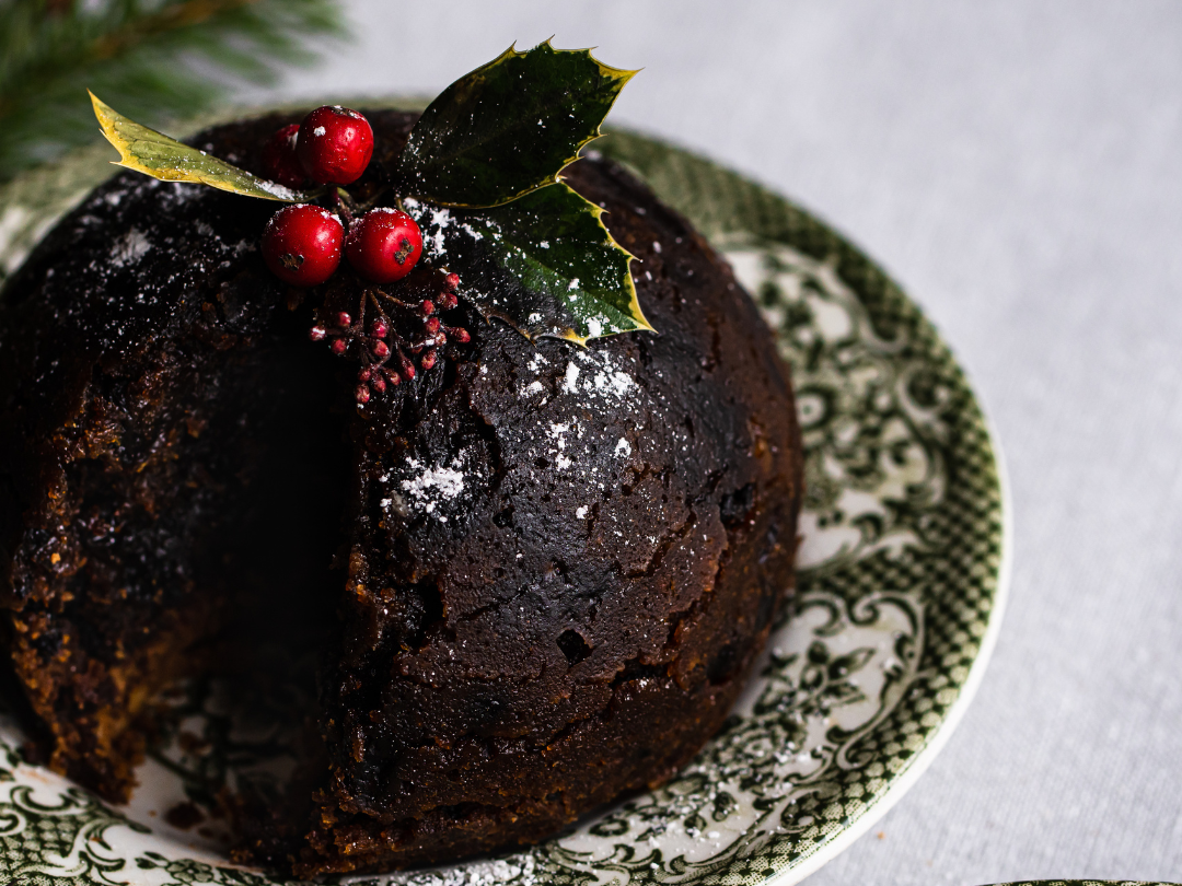 Traditional Christmas pudding topped with holly and berries on a patterned plate