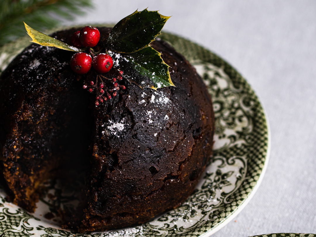 Traditional Christmas pudding topped with holly and berries on a patterned plate