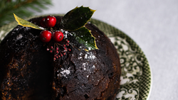 Traditional Christmas pudding topped with holly and berries on a patterned plate