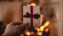 Hand holding a small gift wrapped in plaid paper with a red ribbon and bow