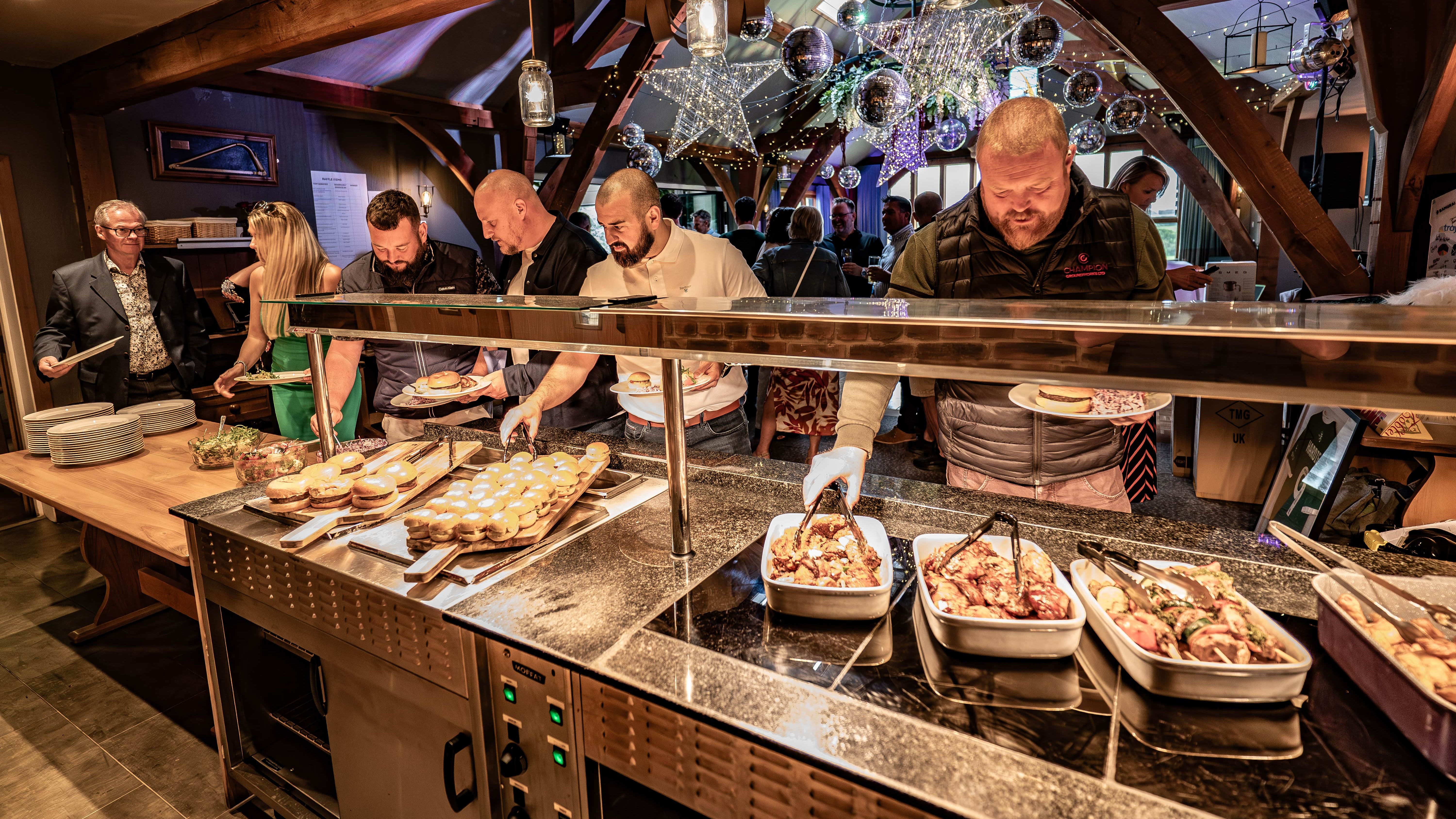 People serving themselves food at a buffet during an indoor celebration event.