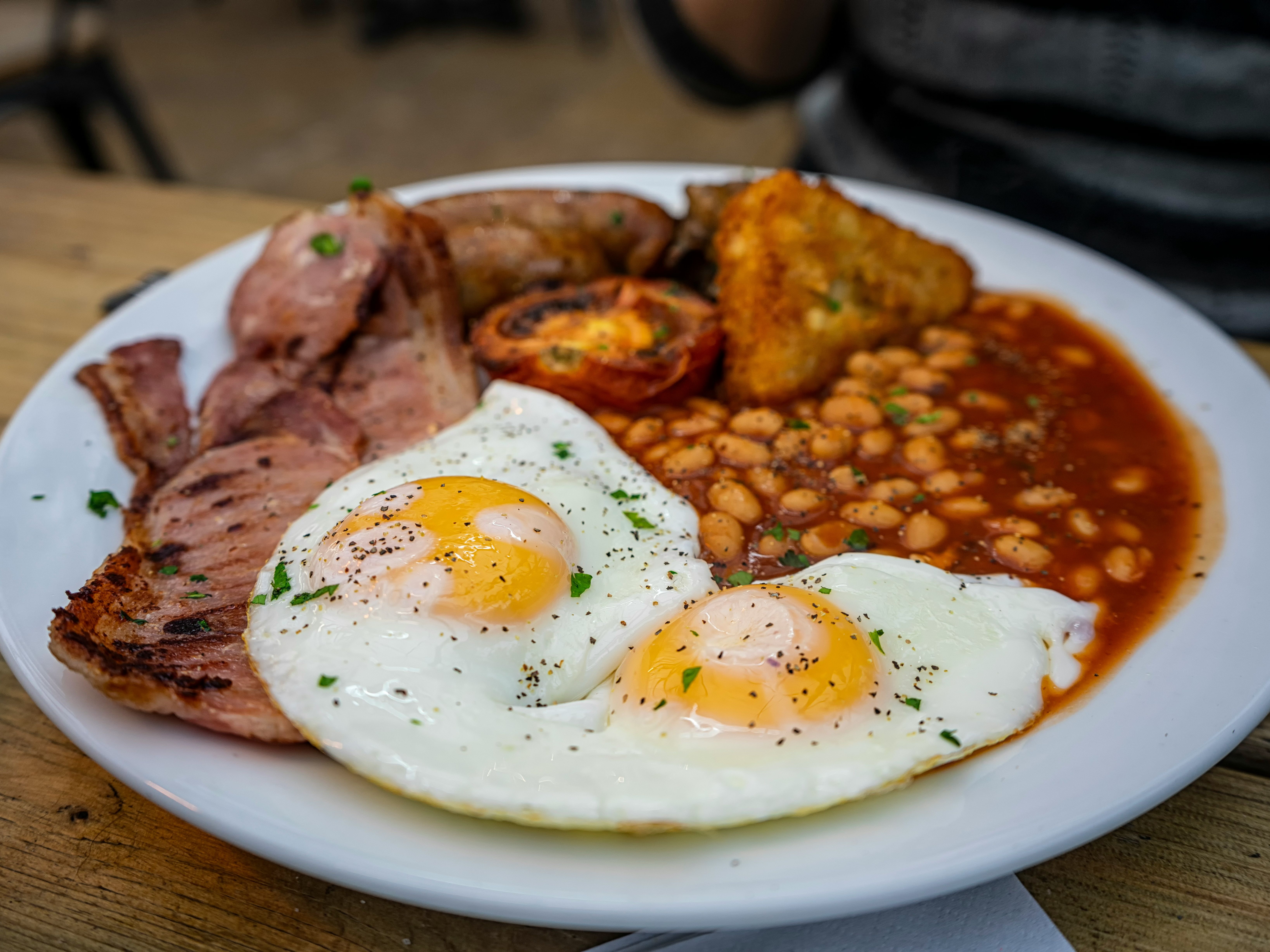 Full English breakfast plate with eggs, bacon, beans, sausage, grilled tomato, and hash brown