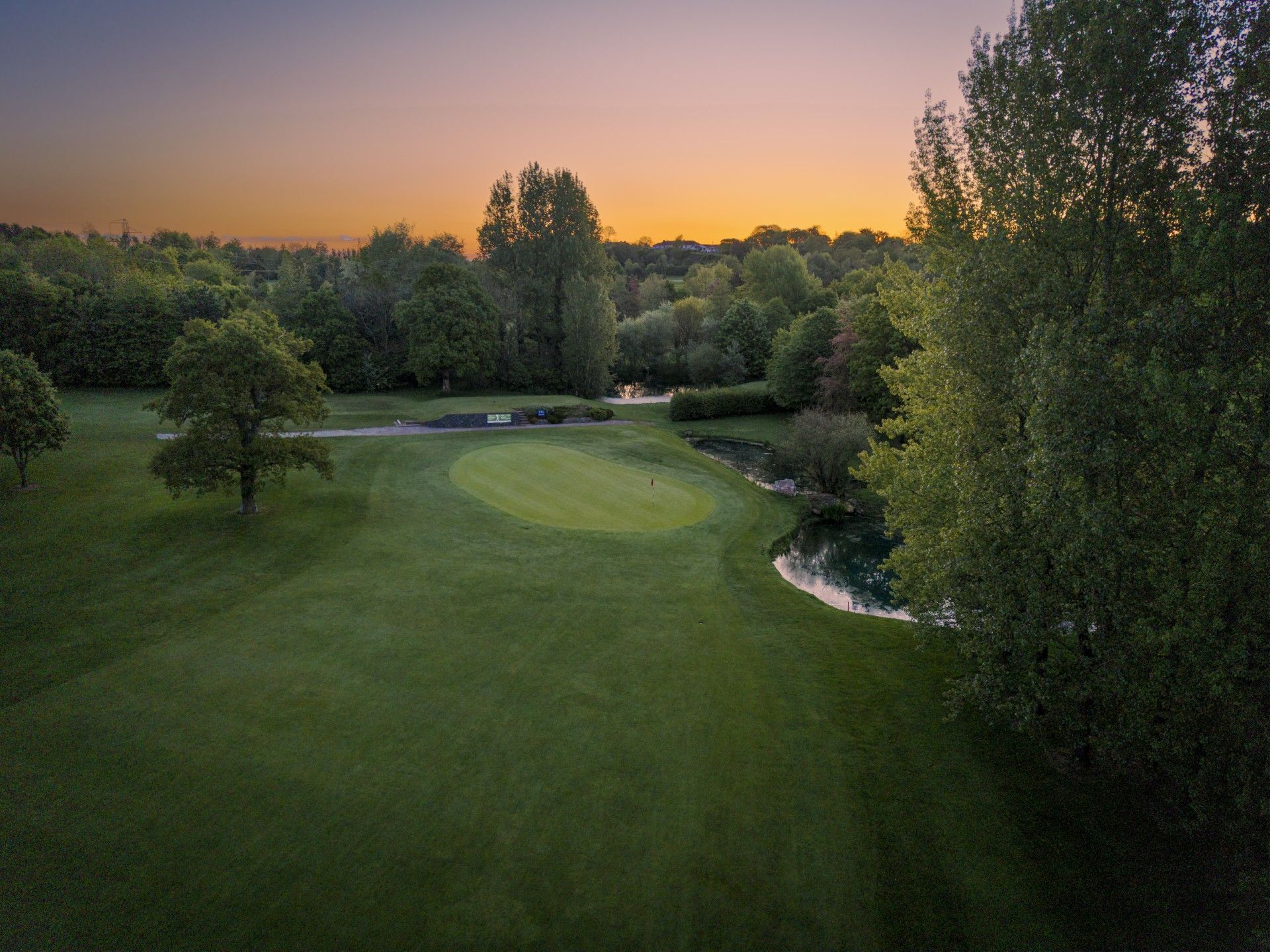 Aerial view of a golf course green surrounded by trees at sunset.