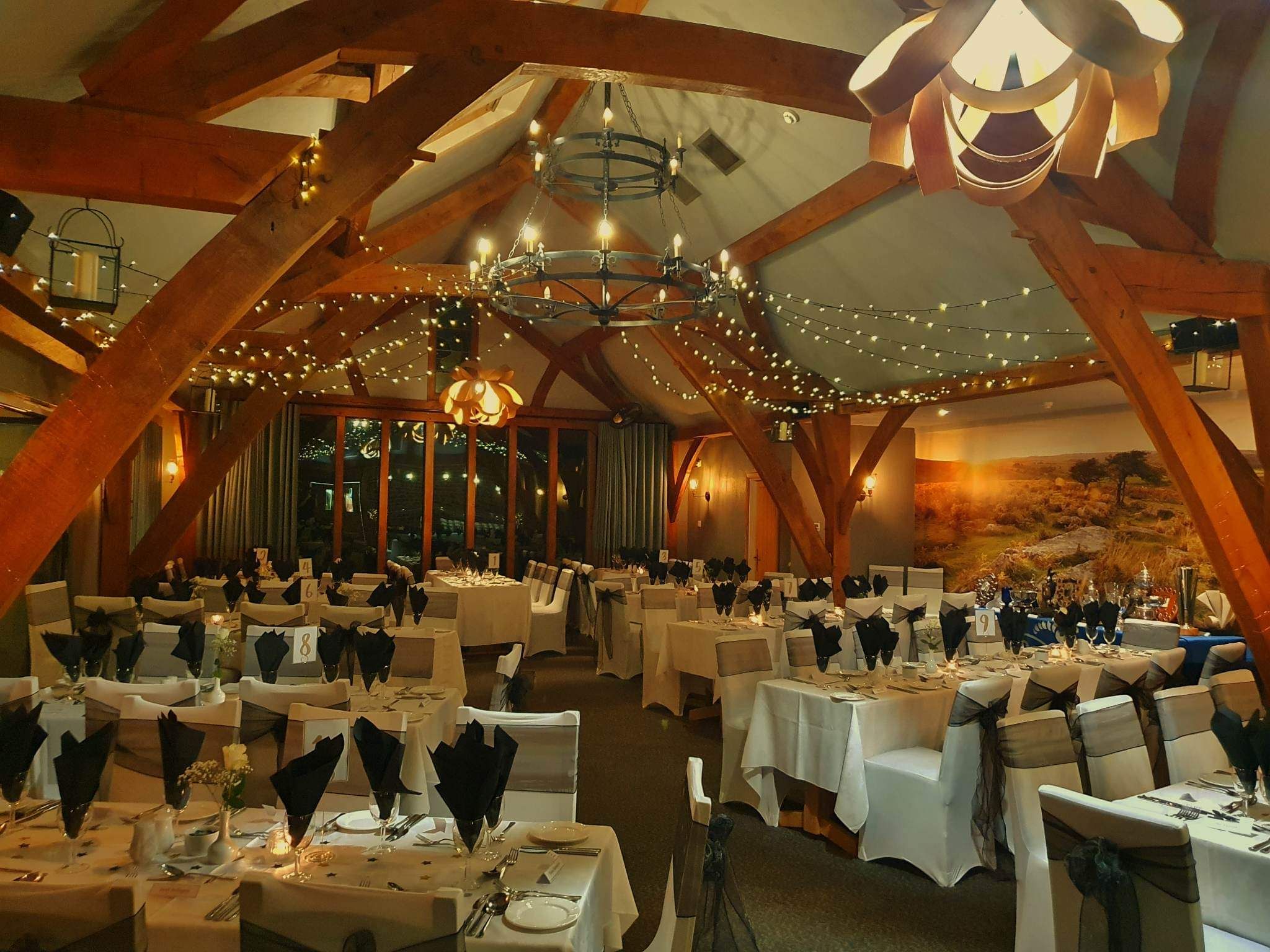 Rustic timber-beamed banquet hall set for a formal dinner with fairy lights and chandeliers