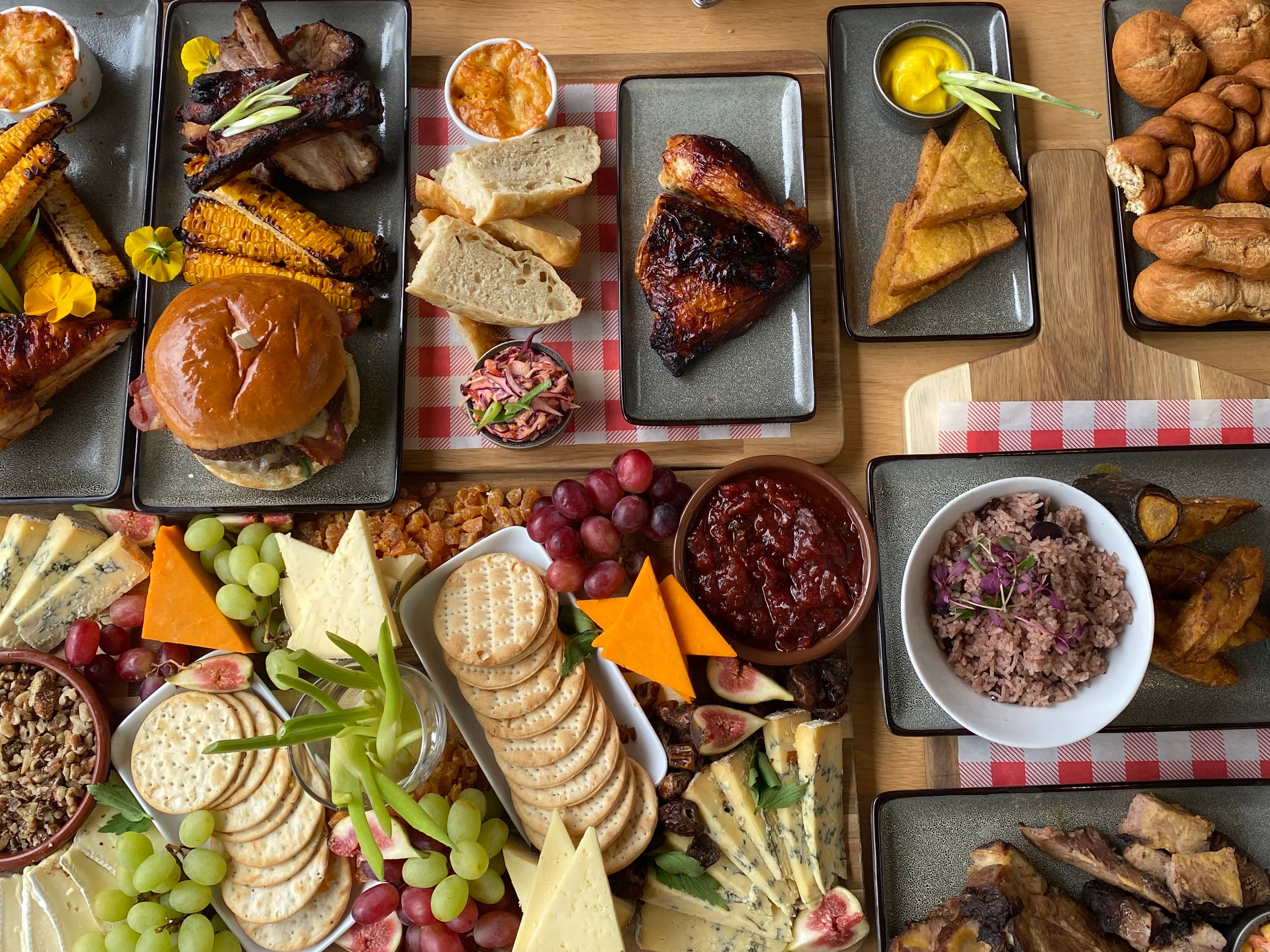 Overhead view of a large sharing platter with grilled meats, bread, chips, olives, cheeses, crackers, grapes and desserts on a wooden table