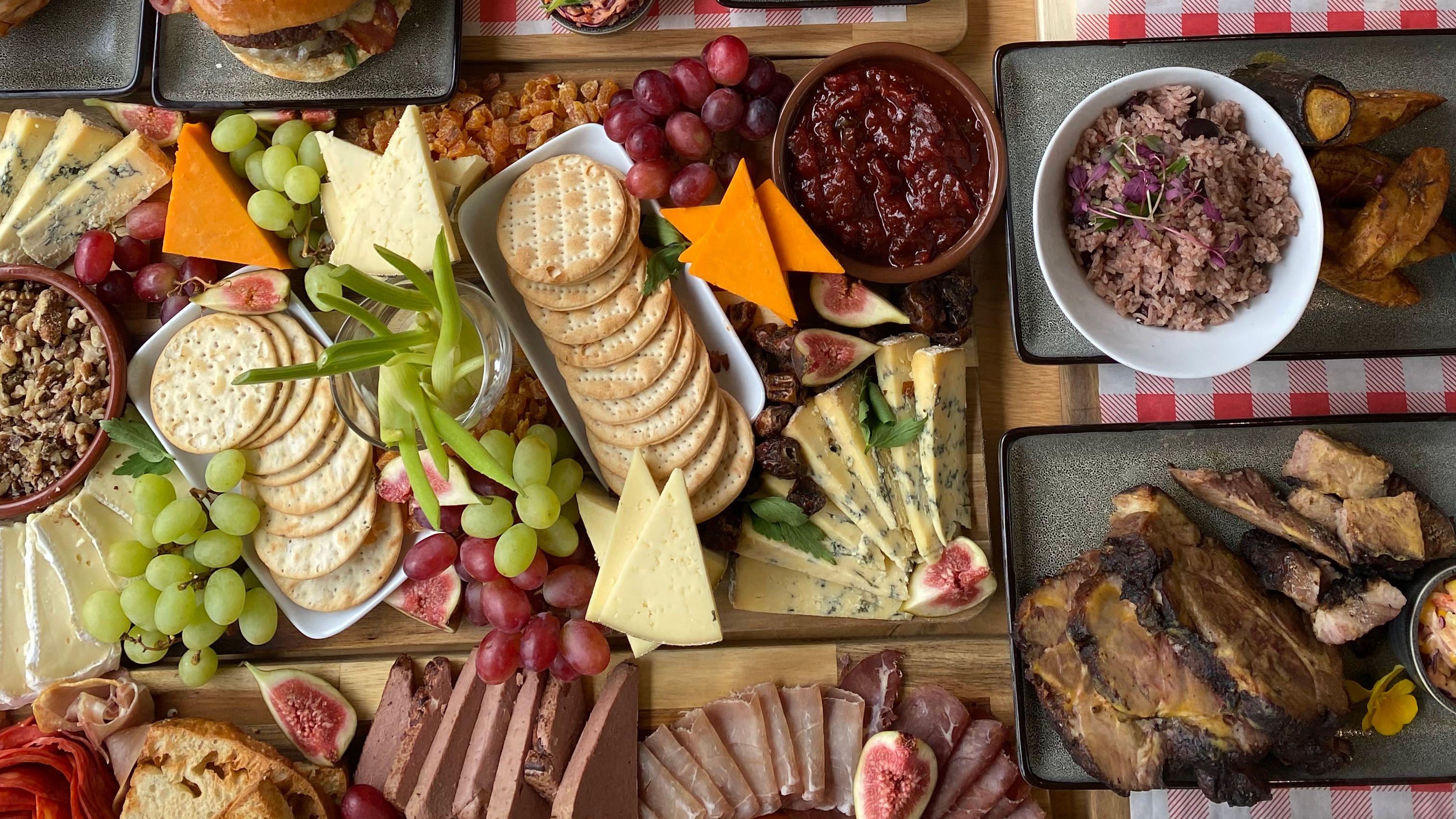 Overhead view of a large sharing platter with grilled meats, bread, chips, olives, cheeses, crackers, grapes and desserts on a wooden table