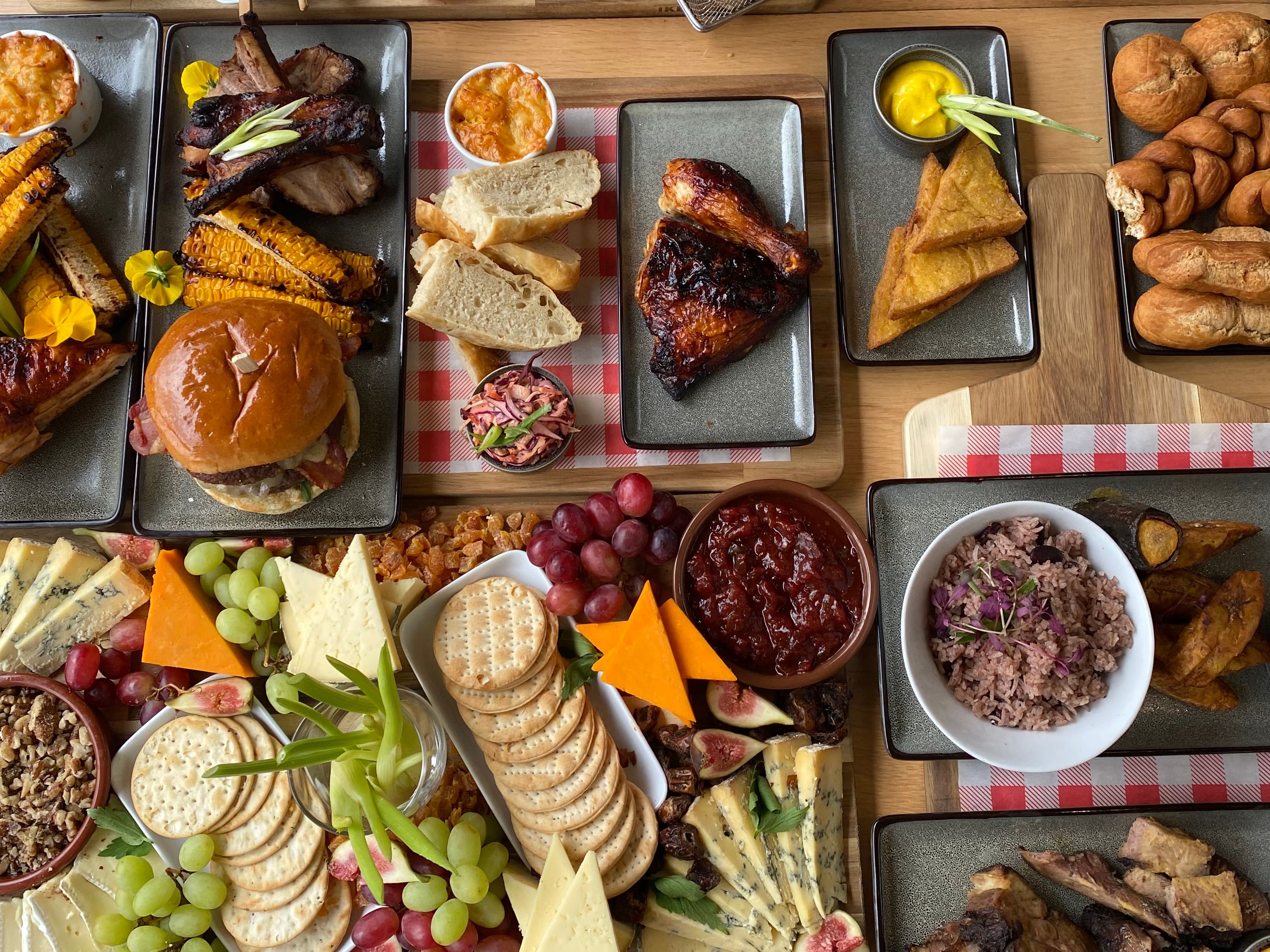 Overhead view of a large sharing platter with grilled meats, bread, chips, olives, cheeses, crackers, grapes and desserts on a wooden table