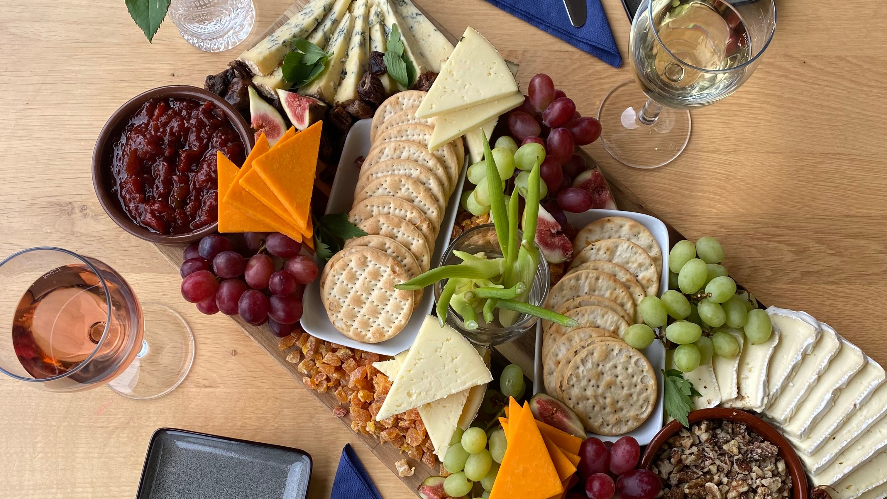 Cheese and cracker sharing board with grapes, figs, chutney and wine on a wooden table