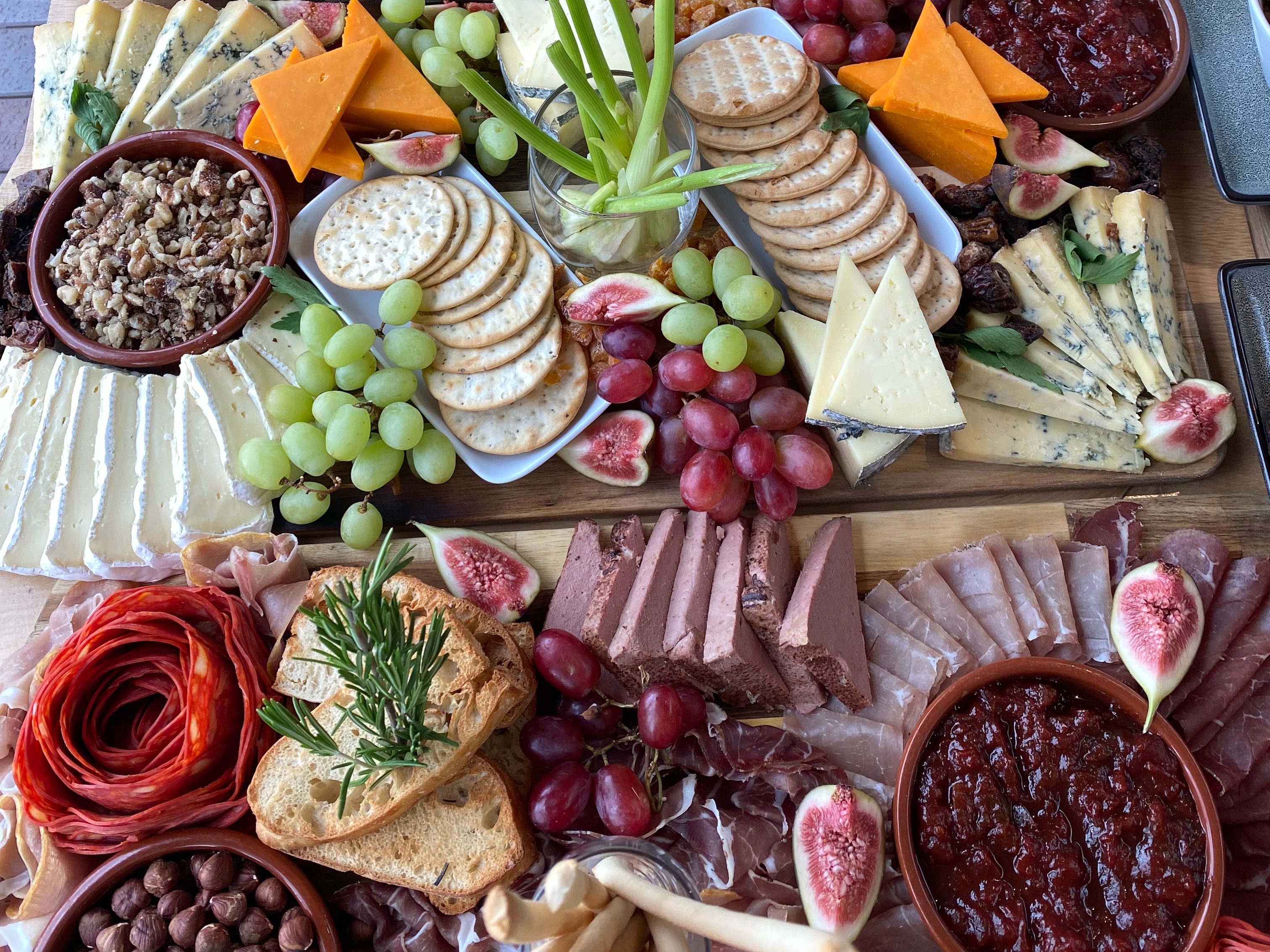 Sharing platter with barbecue meats, burger, cheese board, crackers, grapes and figs on a wooden table