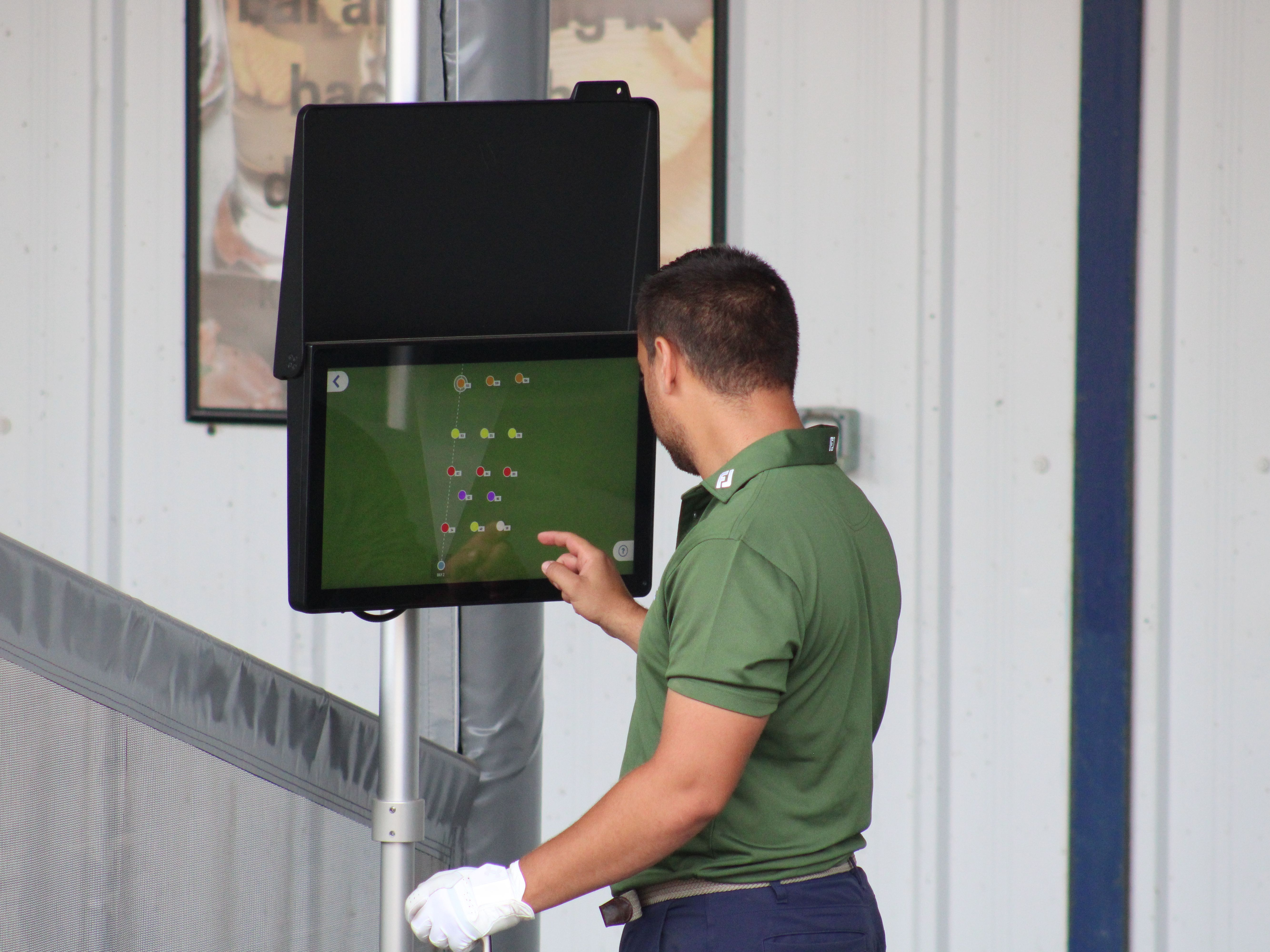 Golfer using a touchscreen launch monitor showing shot data at a driving range