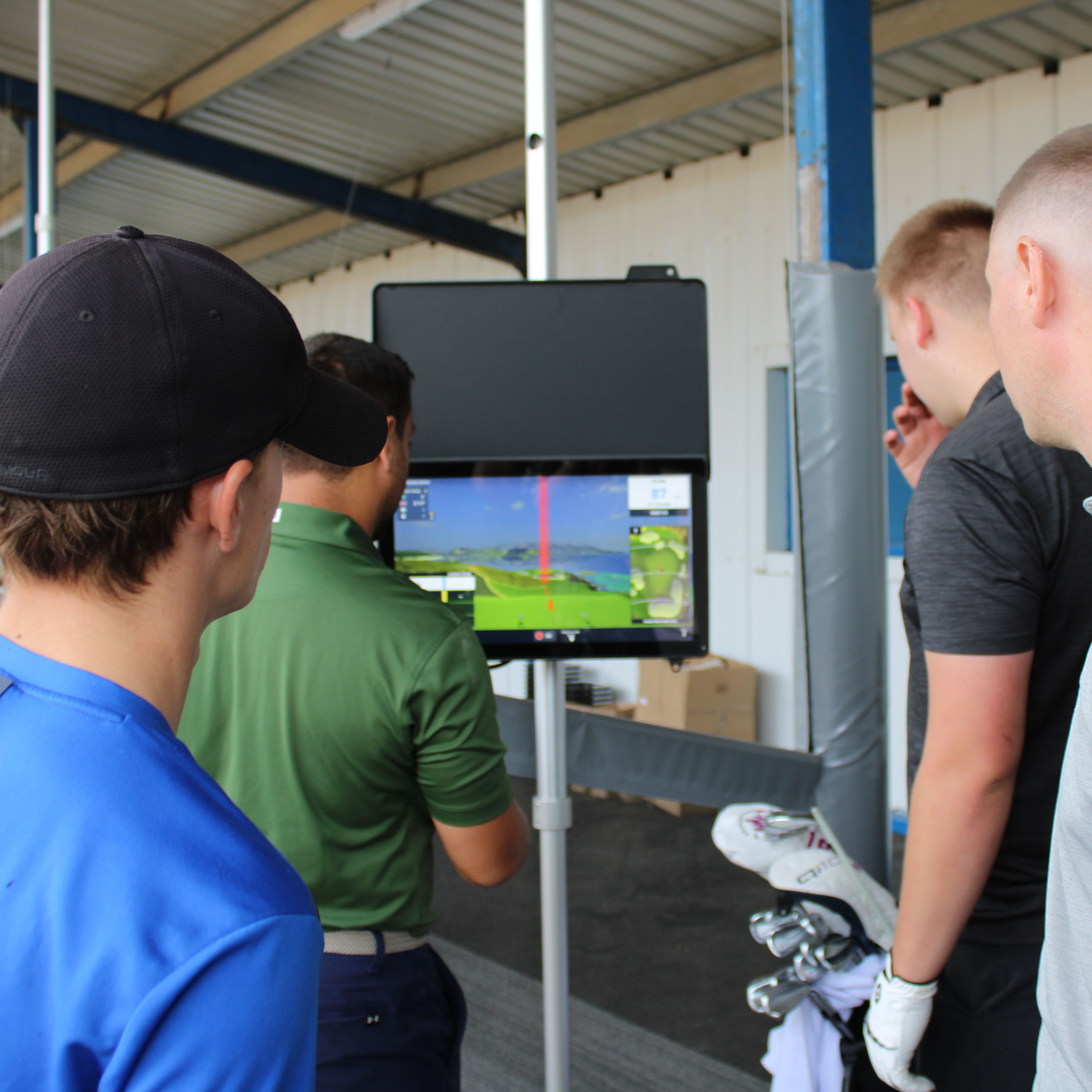 Group of golfers watching a launch monitor screen at an indoor driving range