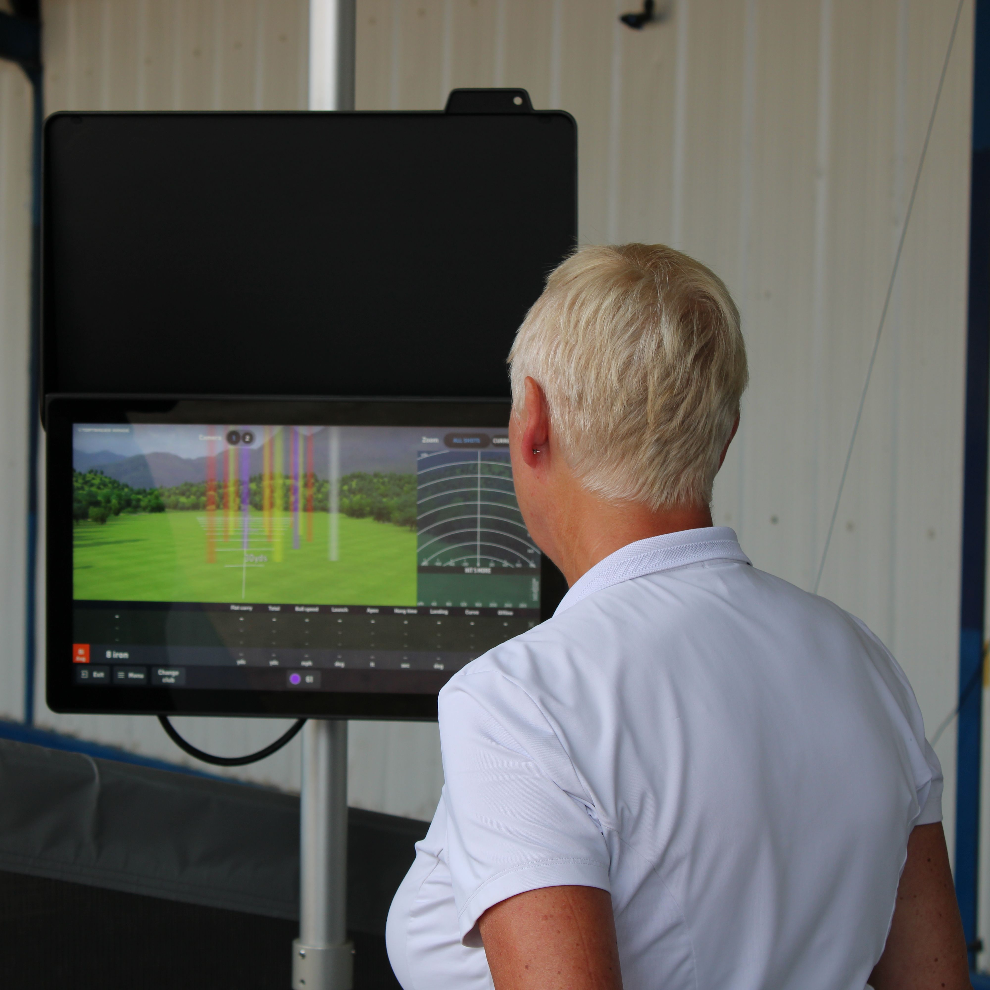 Two people reviewing golf swing data on a launch monitor screen indoors