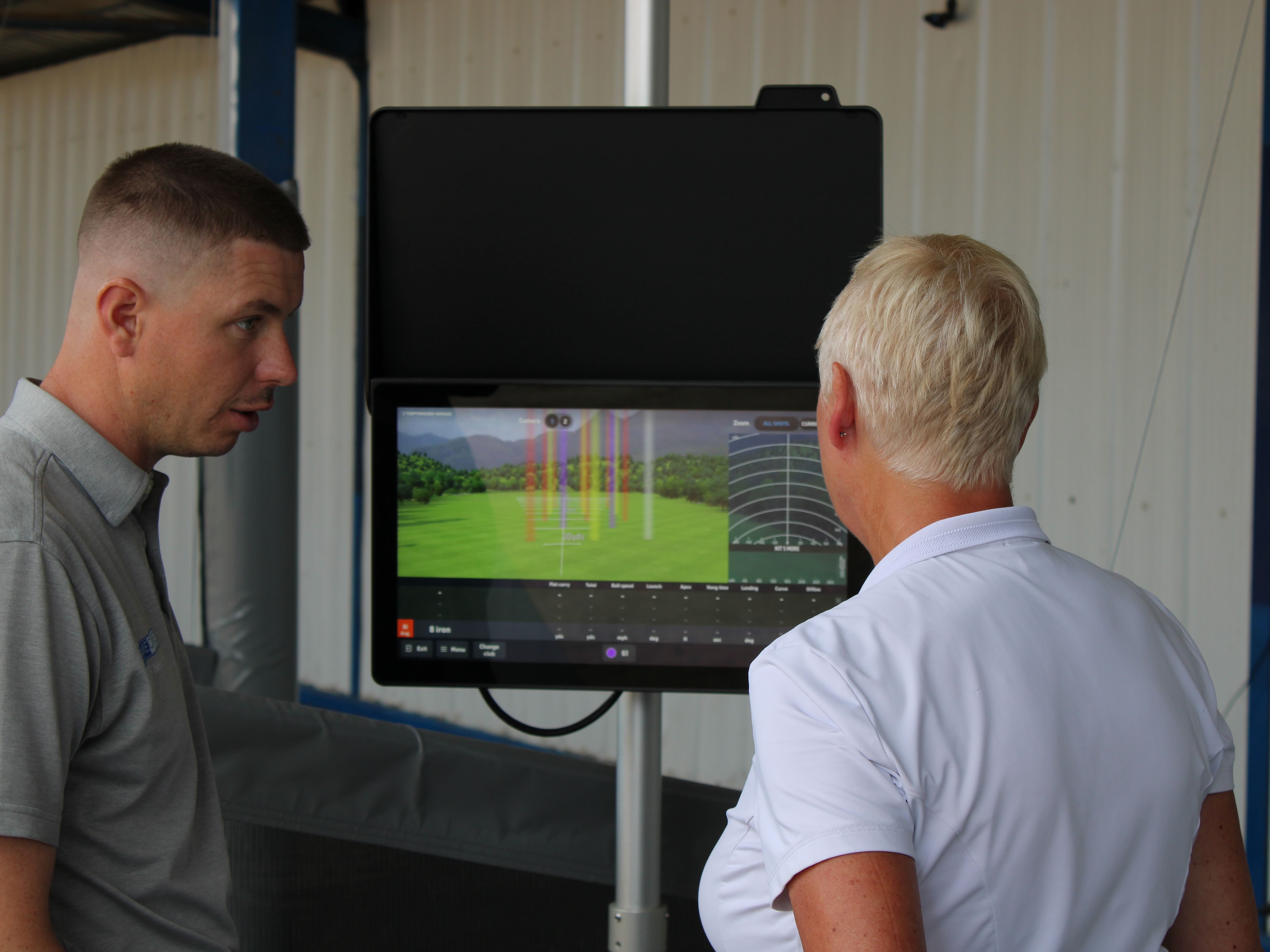 Two people reviewing golf swing data on a launch monitor screen indoors