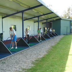 People practicing their golf swings at an outdoor driving range under a metal roof