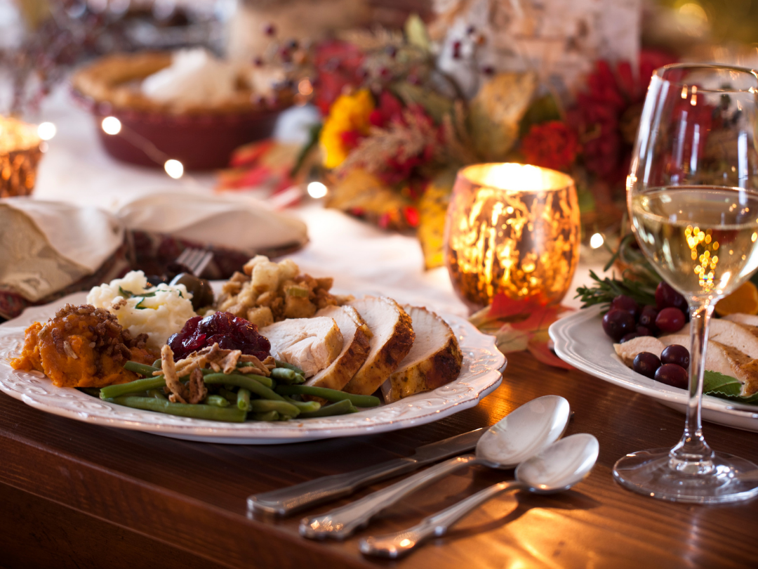 Festive dinner plate with sliced roast turkey, cranberry sauce and green beans on a candlelit table with fairy lights and a glass of white wine